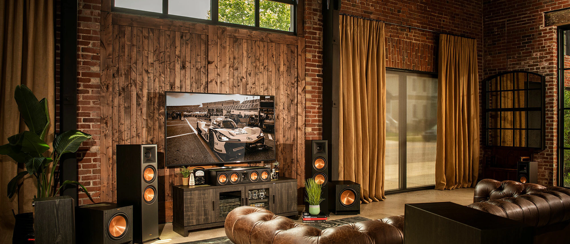 A modern living room home theater featuring a large screen surrounded by high-end Klipsch reference speakers, with ambient lighting that creates a cinematic atmosphere.