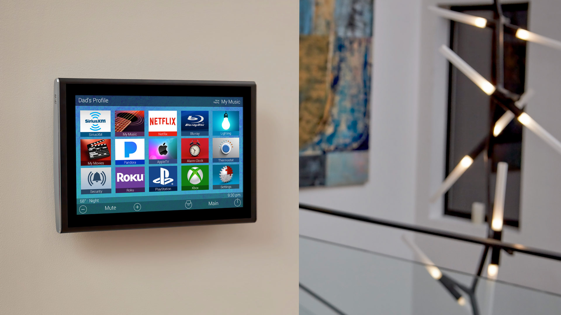 Wall-mounted smart-home touch panel showing colorful app icons for media, lighting, security, and more on a neutral wall; abstract artwork and a modern sculptural light fixture are softly blurred in the hallway beyond.